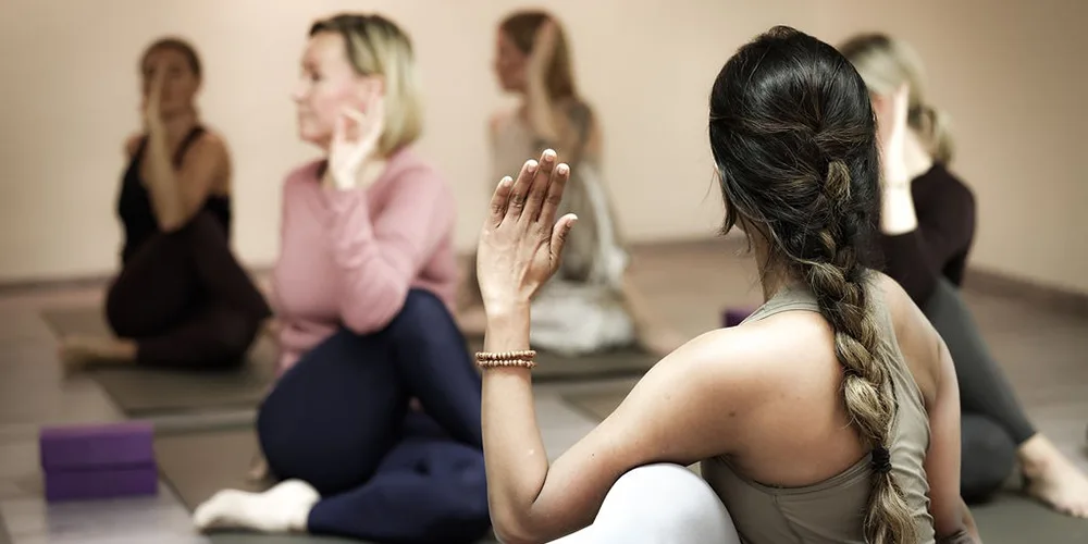 Ryhmä oletettuja naisia tekee istuen kiertoliikettä joogamatolla rauhallisessa studiossa, käsi nostettuna kierron suuntaan.